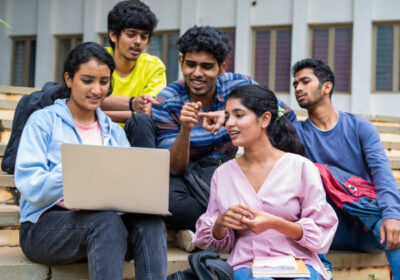 Group of happy students checking results on laptop while sitting on college campus - concept of education, technology and project work discussion